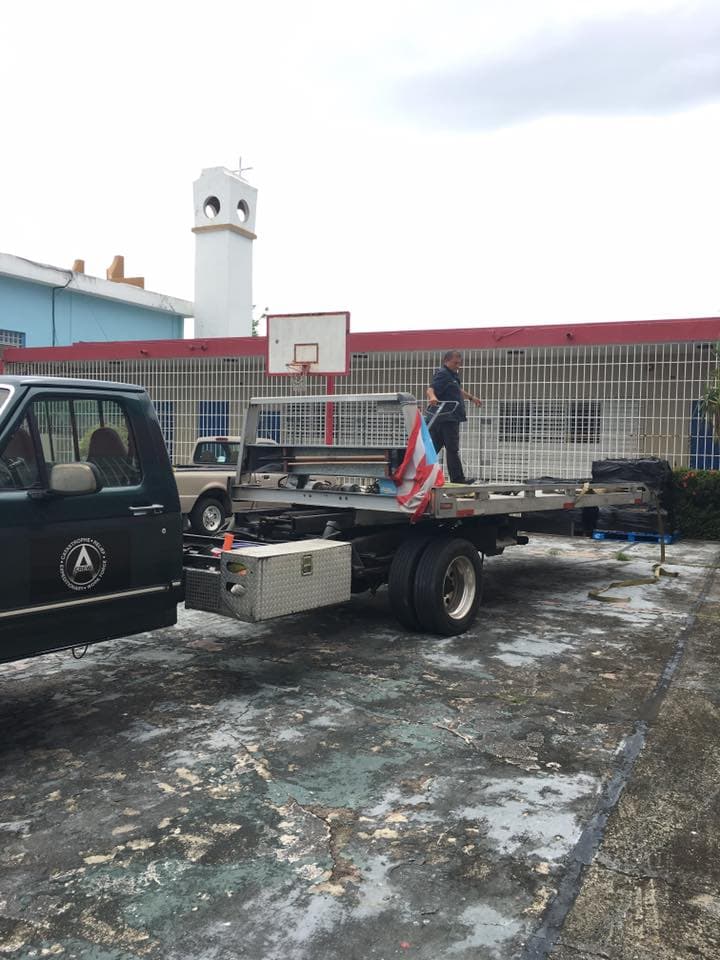 CREW flatbed truck at a school courtyard with basketball hoop, crew member on the bed with a Puerto Rico flag