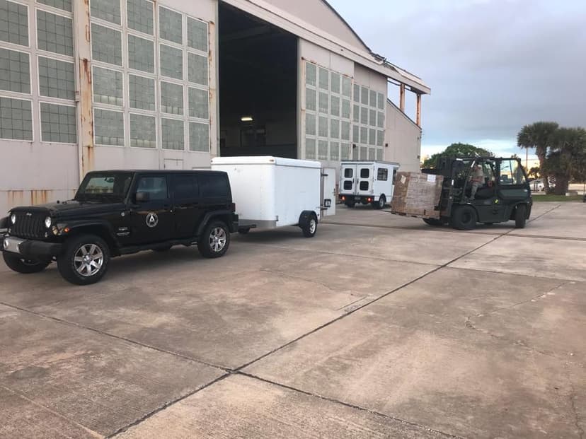 Black CREW Jeep with white enclosed trailer outside the hangar, Air Force forklift loading pallets in the background