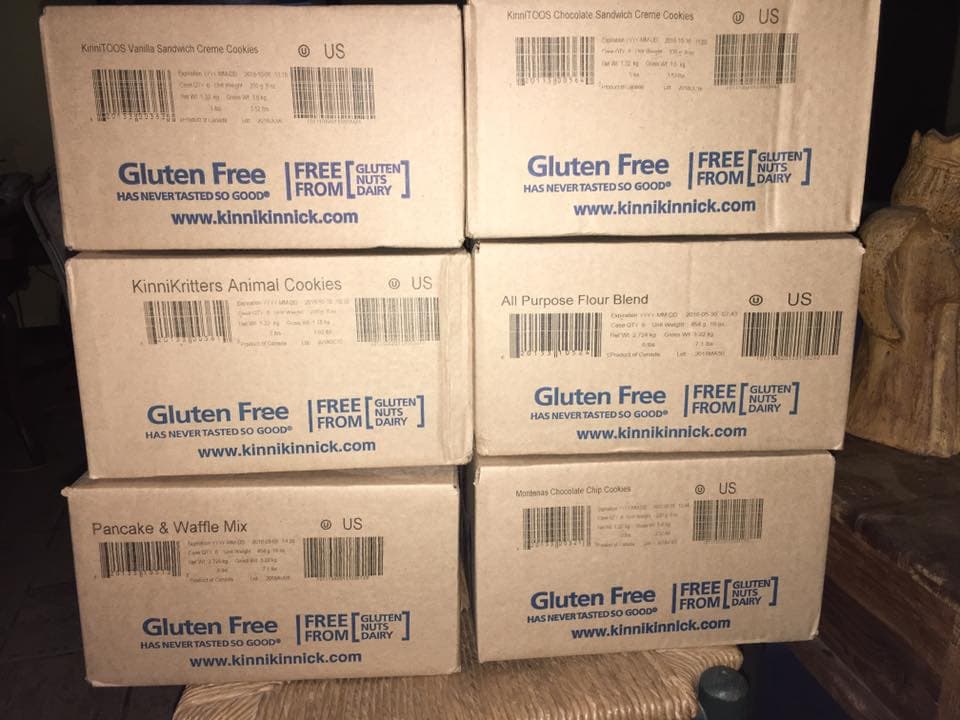 Stack of Kinnikinnick gluten-free boxes — vanilla cookies, animal cookies, flour blend, pancake mix, and chocolate chip cookies